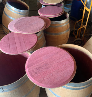 Stack of wine barrels with pinkish-red tops in a storage area.
