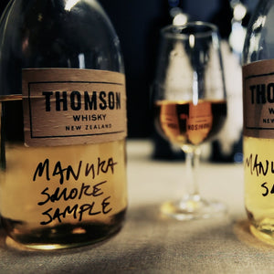Two bottles of Thomson Whisky with 'Manuka Smoke Sample' labels on a table.