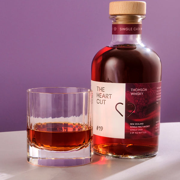 Bottle of 'The Heart Cut' whisky and a glass with whisky on a purple background
