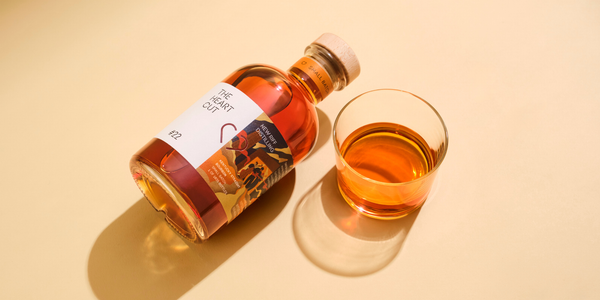 Bottle of #22 The Heart Cut New Riff next to a glass of whisky with a beige background