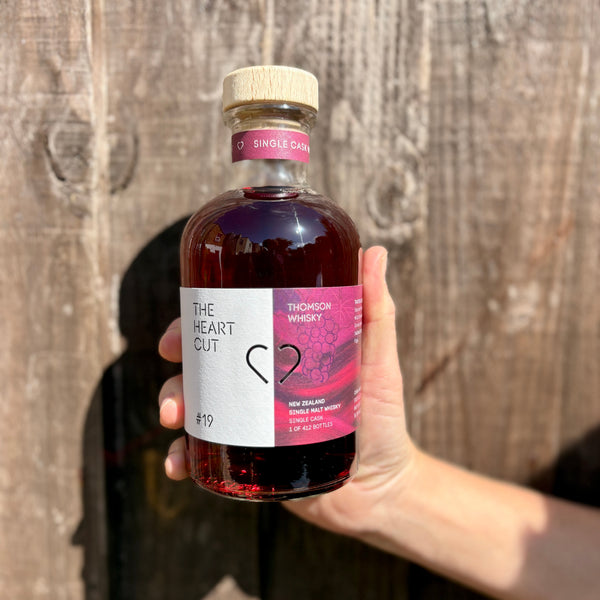 Bottle of 'The Heart Cut' whisky held in front of a wooden background

