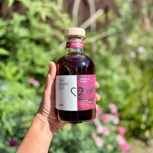 Hand holding a bottle of 'The Heart Cut' against a blurred natural background

