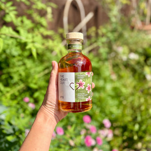Hand holding a bottle of 'The Heart Cut' whisky with a garden background