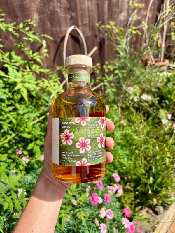 Hand holding a bottle of New Zealand whisky with a garden background