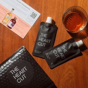 The Heart Cut products on a wooden surface with a glass of amber liquid and a card.