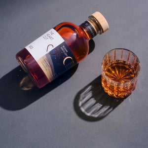 The Heart Cut #23 Boann Distillery whiskey bottle lying on its side next to a filled crystal rocks glass, shot from above on a grey background