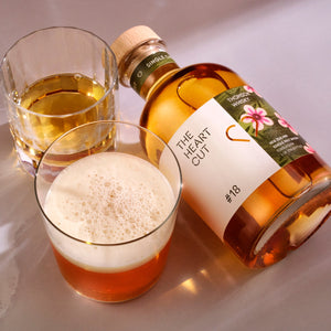 Bottle of 'The Heart Cut' with two glasses of a golden liquid on a white background